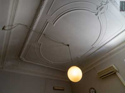 Una stanza, adibita ad uffici, mostra un soffitto impreziosito da modanature bianche con motivi vegetali e stemmi negli angoli